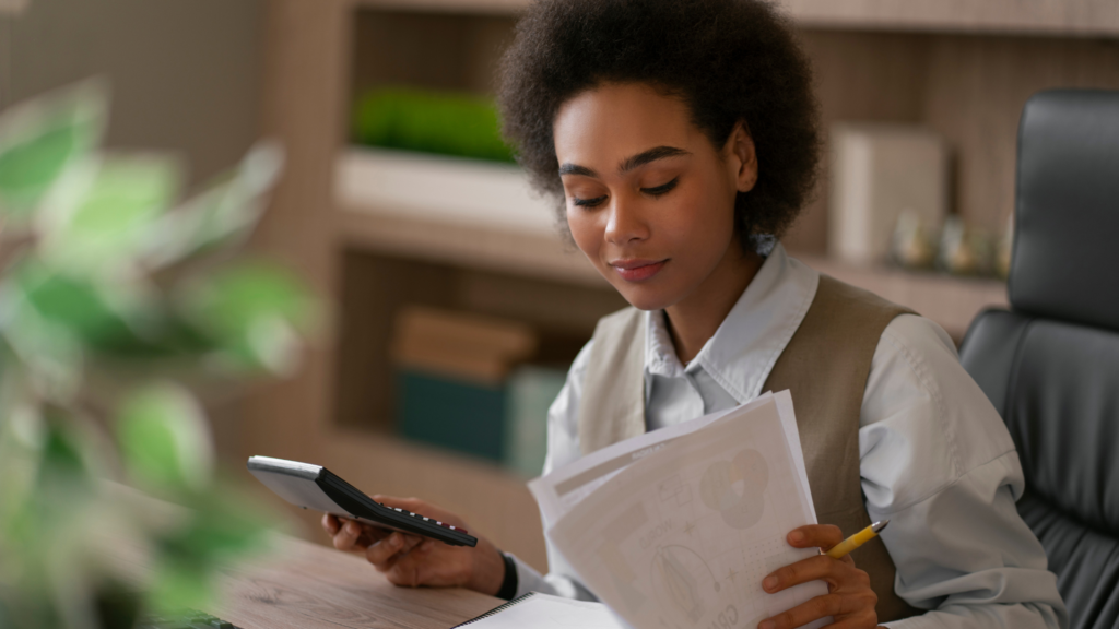 Mulher jovem em um escritório analisando documentos e usando uma calculadora, representando o processo de emissão de nota fiscal eletrônica (NF-e). A imagem transmite a ideia de como emitir nota fiscal com organização e eficiência no ambiente de trabalho.